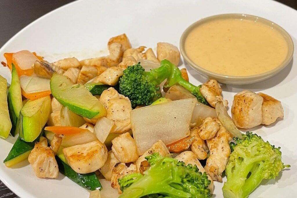 Hibachi chicken with broccoli, zucchini and onion on a white plate